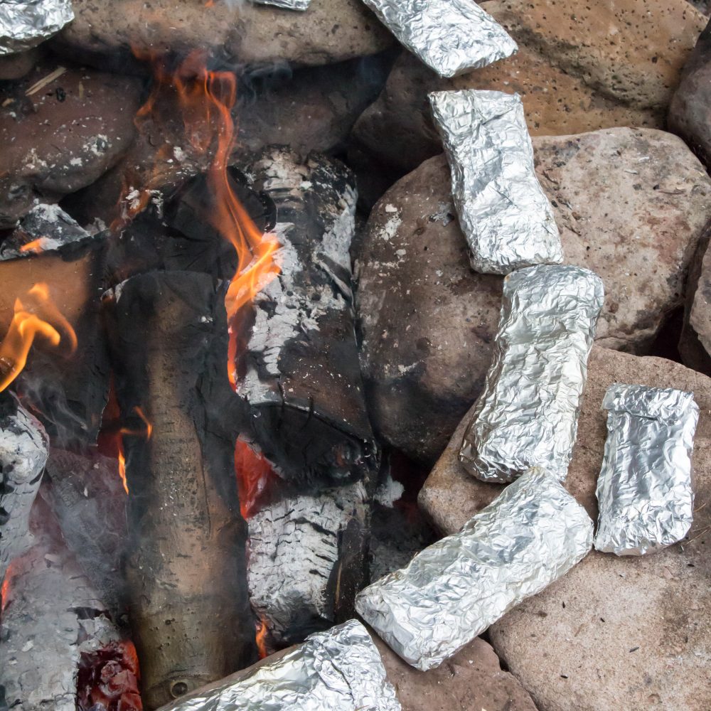Campfire cooking - foil wrapped dinner cooking around a fire